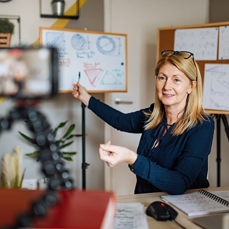 Frau zeigt auf Zeichnung auf Whiteboard und wird von ihrem Smartphone aufgenommen