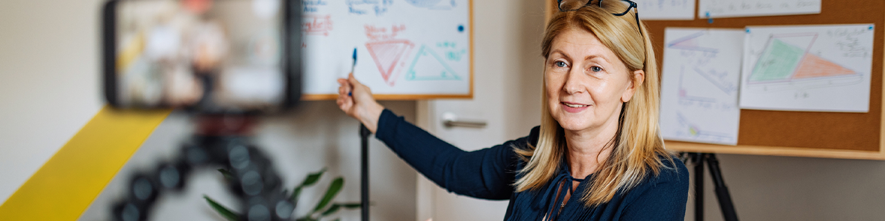 Frau zeigt auf Zeichnung auf Whiteboard und wird von ihrem Smartphone aufgenommen